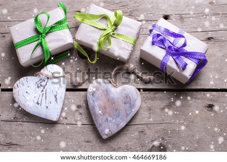 Christmas background with snow effect. Gift boxes with presents and  rustic decorative hearts on aged wooden planks. Selective focus. 
