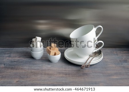 White china porcelain dishes on a wooden table with flower of lily. Two cups stacked with tea spoons. Special light. Toned image.