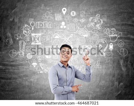 Man in shirt standing in front of blackboard with abstract sketches on it pointing his finger at one of icons. Concept of mind map drawing to find solution.