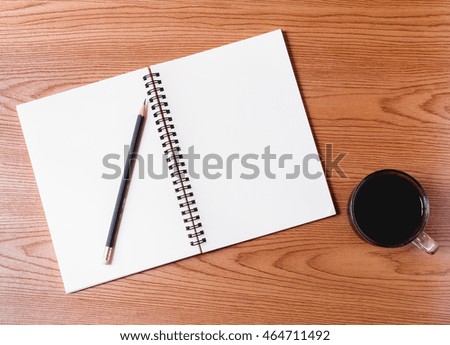 Notebook with pencil and cup of coffee on wooden table.