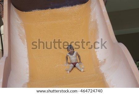 Happy boy in water park sliding down on orange color water slider. Summer,vacation, childhood.