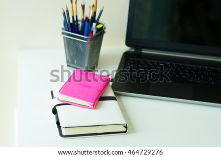 Two notebooks of pink and white color, office stationery and black laptop on white office table