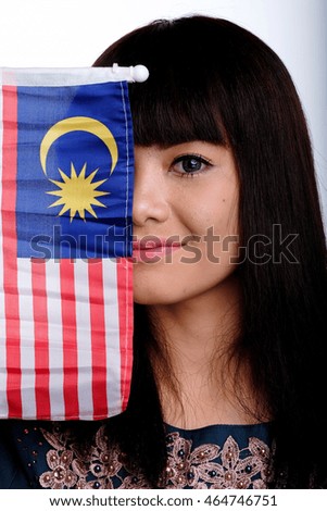 A pretty malay woman wearing traditional dress is smiling while holding a Malaysian flag isolated in white background