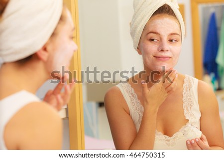Woman applying mask moisturizing skin cream on face looking in bathroom mirror. Girl taking care of her complexion layering moisturizer. Skincare spa treatment. 