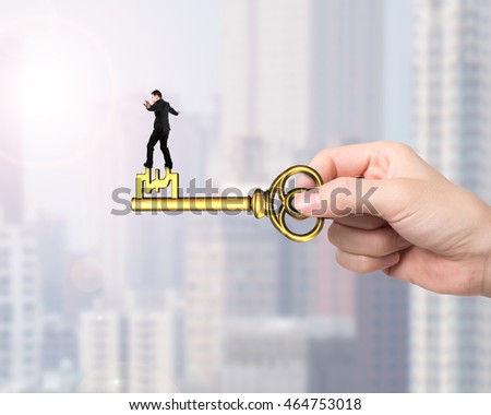 Man balance on treasure key in pound sign shape with hand holding, on city buildings background.