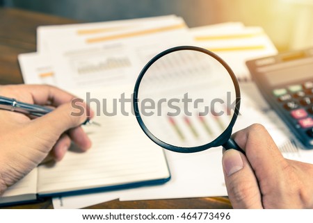 Man hand holding magnifying glass analyzing business financial data. Photo with sunlight filter effect. Royalty-Free Stock Photo #464773496