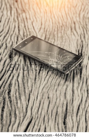 Mono tone photo smartphone with broken screen on wood background,broken touch screen of mobile phone on a wooden board.