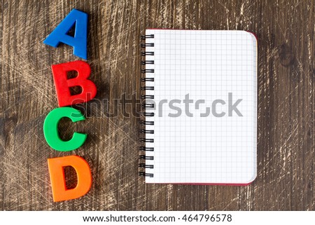 ABCD spelling from plastic letters and blank notebook on wooden background
