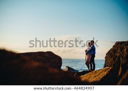 Couple admires a sunset standing by the sea on the stones Royalty-Free Stock Photo #464824907