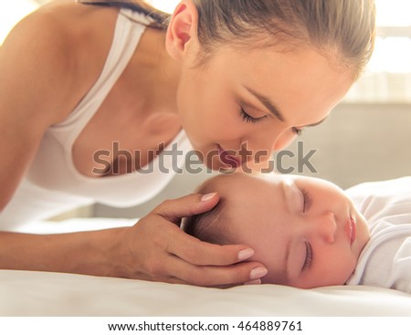 Beautiful young mom is kissing her cute little baby who is sleeping in bed at home, close-up