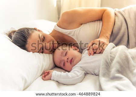 Side view of beautiful young mom and her cute little baby sleeping in bed at home Royalty-Free Stock Photo #464889824