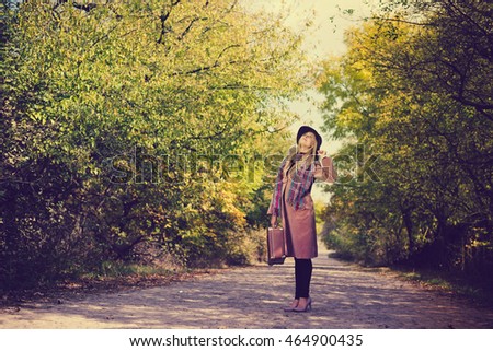 Portrait of woman in hat and coat with suitcase on the road outdoors background