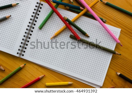 Variegated colored pencils and white square-lined paper notebook on a light orange wooden study table close-up atop
