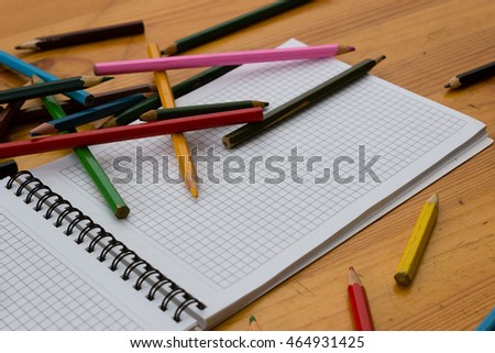 Variegated colored pencils and white square-lined paper notebook on a light orange wooden study table close-up