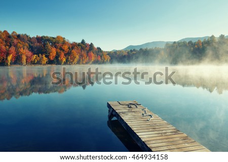Autumn foliage and fog lake in morning with boat dock Royalty-Free Stock Photo #464934158