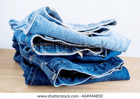 Stack of blue jeans on wooden table.
