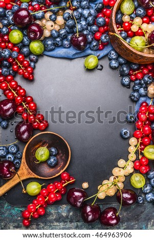 Variety of fresh summer berries with wooden cooking spoon on chalkboard background, top view, frame, vertical