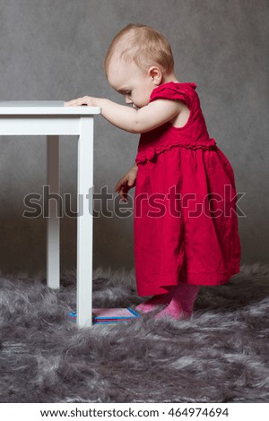 A baby girl dressed in a red pink velvet dress is playing in the studio
