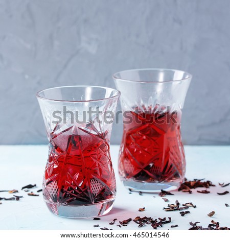 Two traditional asian style glasses with hibiscus tea karkade, served with dry hibiskus over blue and gray textured background. With space for text. Square image