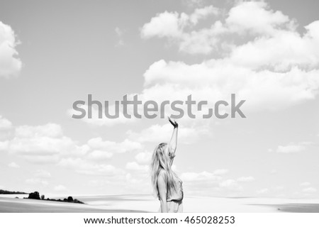 Black and white photography of female lifting arm standing in field over cloudy sky background. Concept of faith. Book cover design