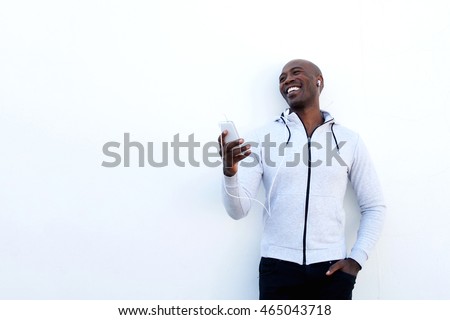 Portrait of smiling young african man with mobile phone and headphones standing against while wall
