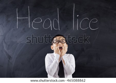 Portrait of a scared male student standing in the classroom while looking at text Head Lice on the chalkboard