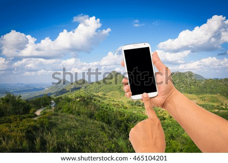 Male hand is holding a modern touch screen phone and blur image of mountain in background