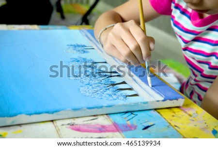 Little Asian girl painting tree and snow with brush and acrylic color, winter landscape picture.