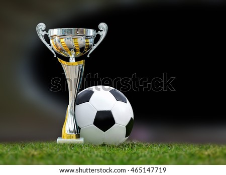 Close golden soccer trophy and ball in green stadium grass 