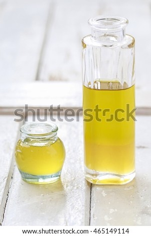Big bottle and small jar of golden liquid on white wooden background. 