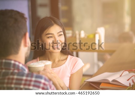 Toned image of romantic couple having date in restaurant or cafe. Happy Asian or Korean lady looking at window and smiling.