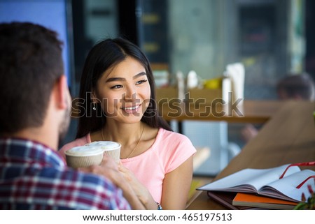 Romantic couple having date in restaurant or cafe. People drinking coffee. Asian or Korean lady looking into window.