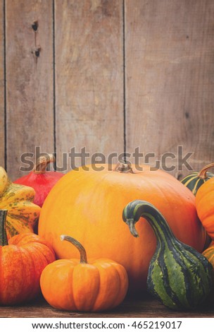 pile of orange pumpkins with fall leaves, copy space on wooden wall, retro toned