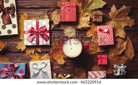 Cup of coffee and season gifts with leafs on wooden background