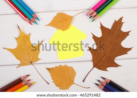 Colorful crayons, paper in shape of building and orange leaves on white boards, back to school in autumn concept
