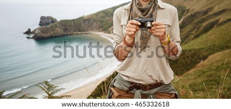 Into the wild in Spain. smiling adventure woman hiker viewing photos on camera in front of ocean view landscape