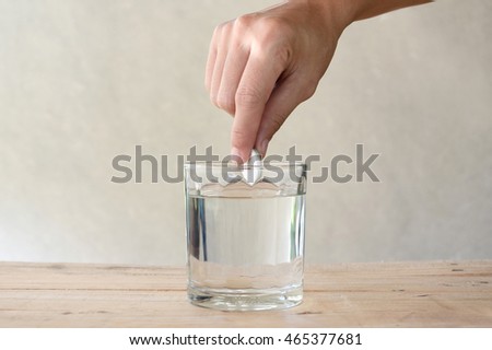 woman put effervescent tablet in glass of water on wooden table
