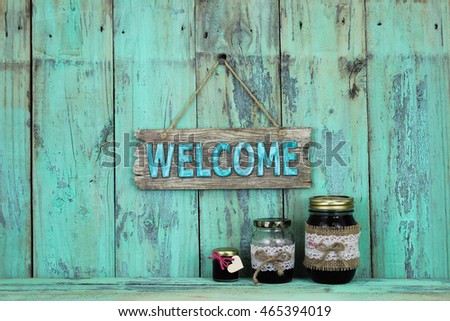 Welcome sign hanging over glass jars of fruit jelly on antique rustic mint green wood background