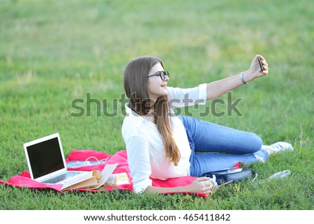 beautiful girl lies with the outdoors with laptop and phone. student working, smiling and doing selfie