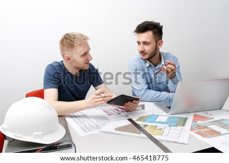 Two young man sit at the table working at a dwelling project