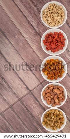 Super food tiger nuts, mulberry berries, cacao beans, goji berries, quinoa seeds, golden berry in white bowls over wooden background.