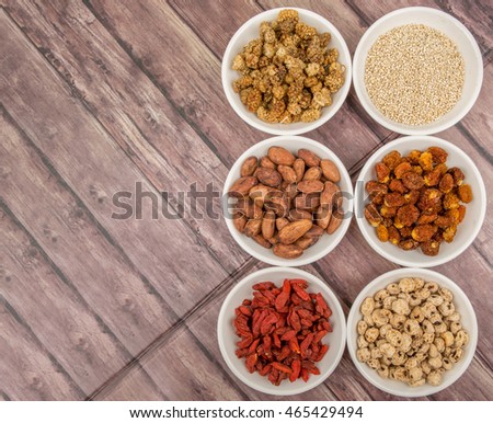 Super food tiger nuts, mulberry berries, cacao beans, goji berries, quinoa seeds, golden berry in white bowls over wooden background.
