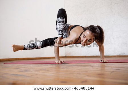 Young beautiful athletic girl practicing indoor yoga asanas. Parivritta Eka Pada Koundinyasana, twisted one legged arm balance posture, Crow variation