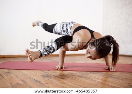 Young beautiful athletic girl practicing indoor yoga arm-balance. Eka Pada Koundiyanasana