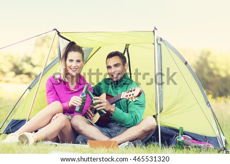 Picture showing couple camping in forest and playing guitar