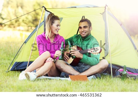 Picture showing couple camping in forest and playing guitar