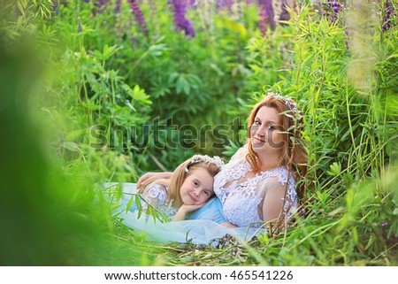 Pregnant woman and daughter lie on the grass in the field with lupine