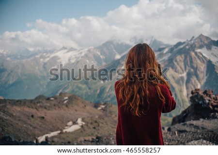 
beautiful young woman with red hair photographer takes a picture of a mountain landscape on the camera while hiking