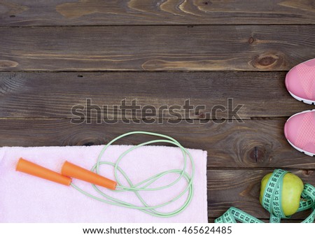 Clothes, objects, accessories for the sport. Running shoes,jump rope, a towel, an Apple, measuring tape and water bottle. The equipment on wooden background.Healthy eating. The place to advertise.