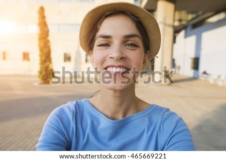 End result selfie picture of a beautiful young woman smiling, while wearing a hat and a blue tshirt on a sunset background